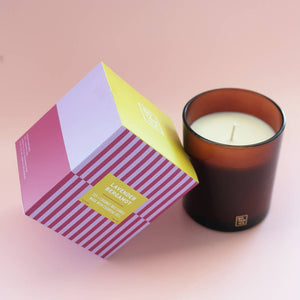 Candle in a brown holder with a striped gift box on a pink background