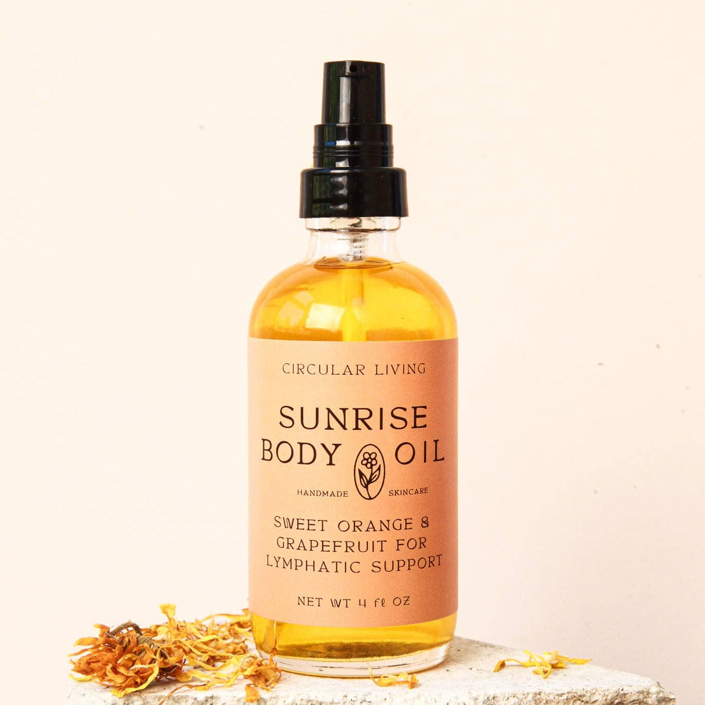 Bottle of Sunrise Body Oil by Circular Living on a stone surface with flowers.