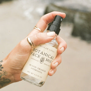 Hand holding a Botanical Face Mist bottle with a blurred natural background