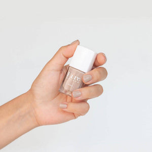 Hand holding a bottle of nail polish with a white cap on a light gray background
