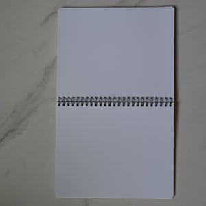 White notebook with a black spiral binding on a marble surface
