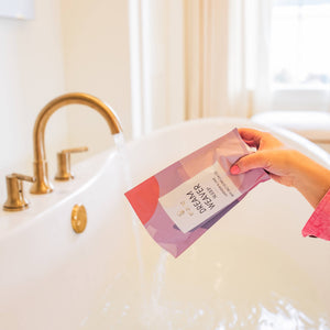Person holding a pink bath bomb in a bathtub with a blurred background