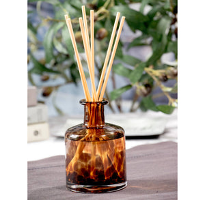 Tortoiseshell-patterned diffuser bottle with wooden sticks on a blurred natural background