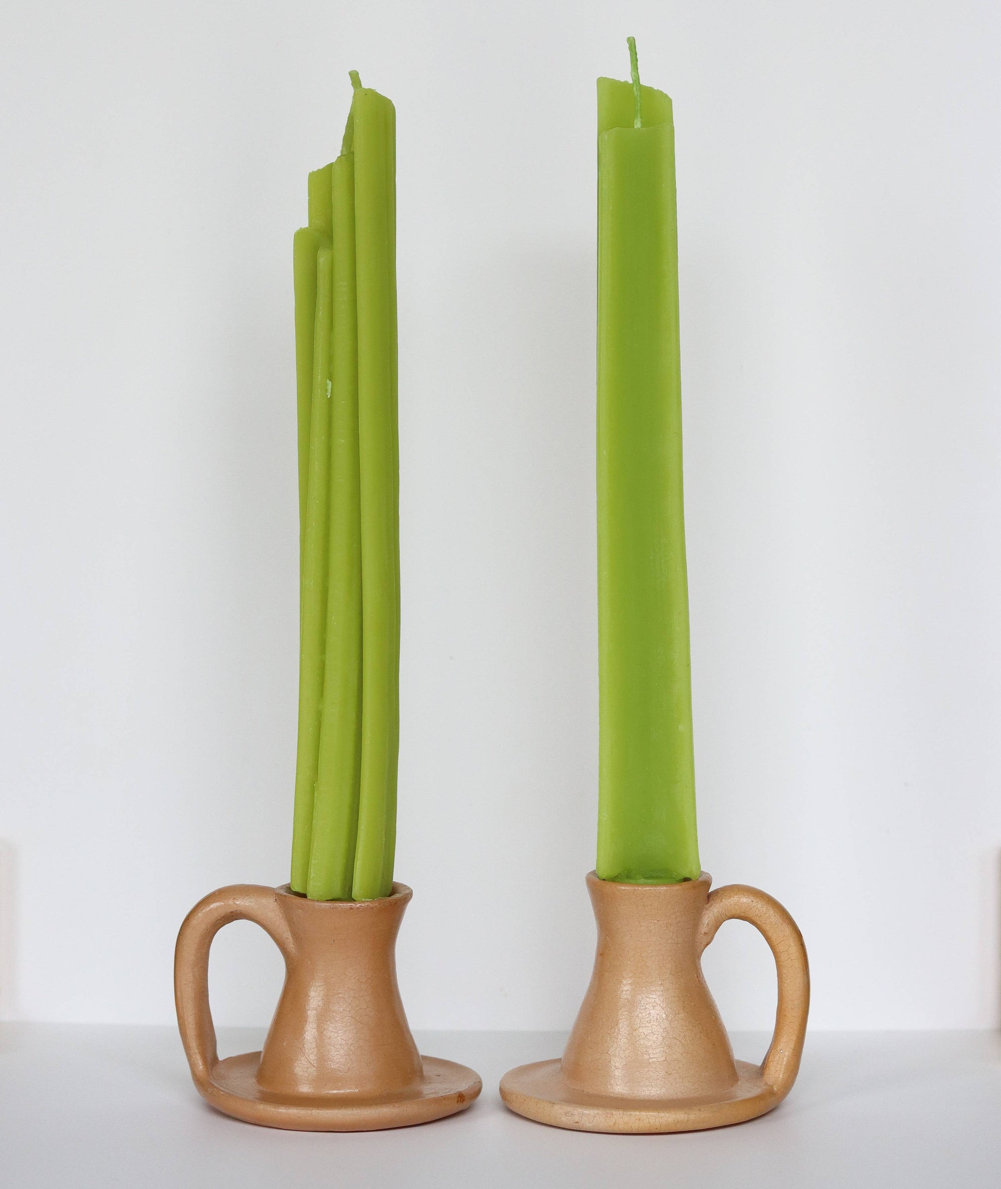 Two green candles in terracotta candle holders on a white background