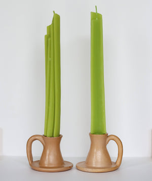 Two green candles in terracotta candle holders on a white background