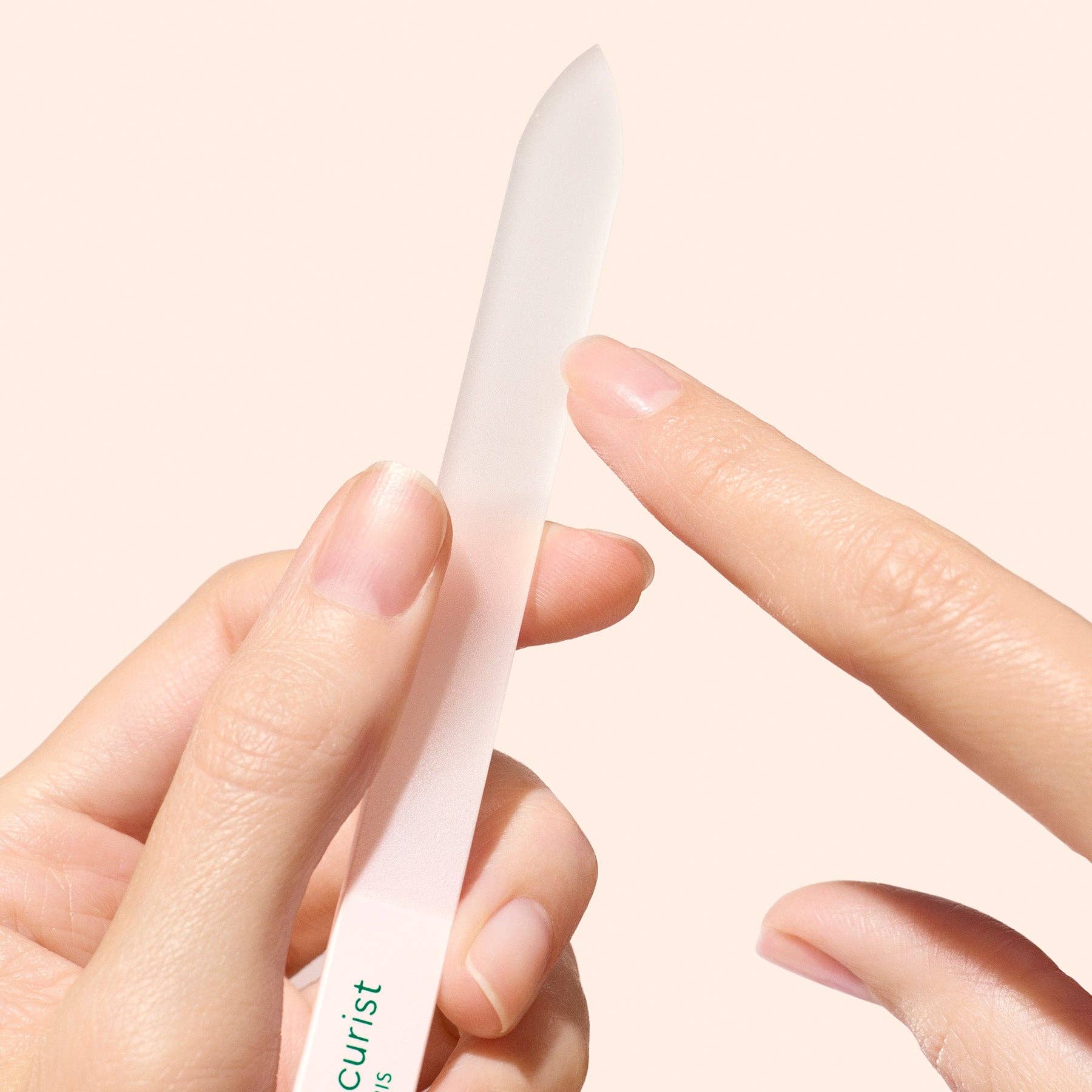 Person holding a white glass nail file with 'manicurist' branding on a light pink background