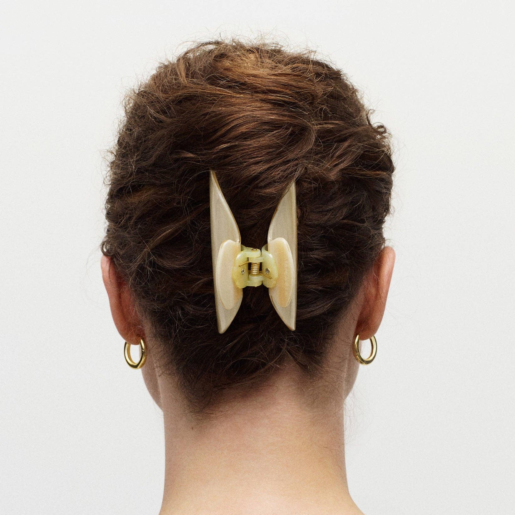 Person with a stylish hair bun featuring a large beige hair clip on a plain background