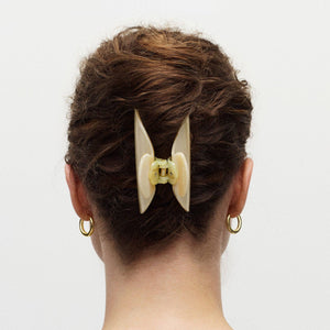 Person with a stylish hair bun featuring a large beige hair clip on a plain background