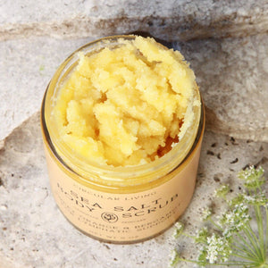 Jar of sea salt body scrub on a stone surface with flowers.