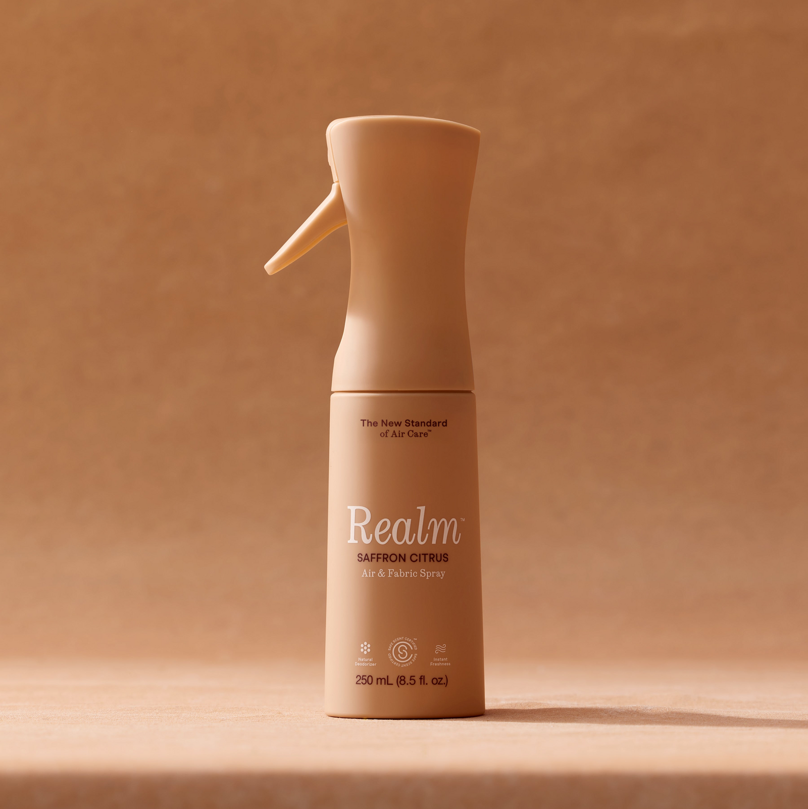 Beige air freshener spray bottle labeled 'Realm' on a brown background