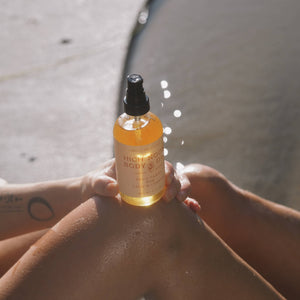 Bottle of body oil held by a person with water in the background