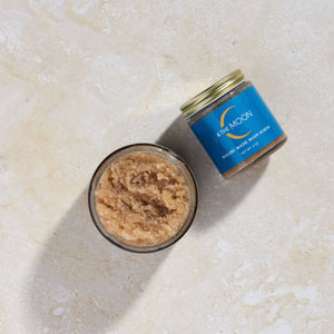 Jar of brown sugar scrub with blue label on a beige surface