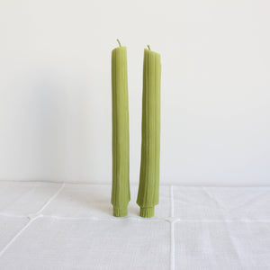 Two green candles on a white tiled floor
