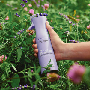 Hand holding a purple bottle labeled 'Realin' amidst a field of flowers