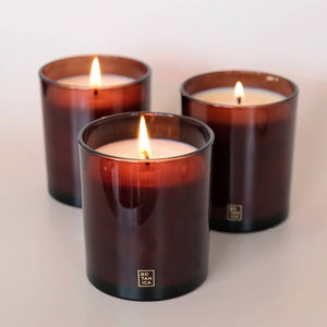Three lit candles in brown glass containers on a light background