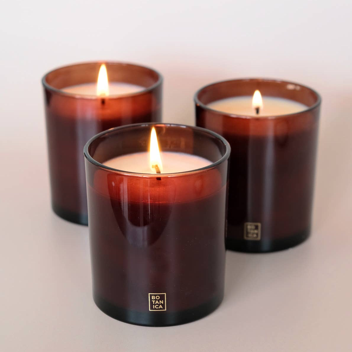 Three lit candles in brown glass containers on a light background