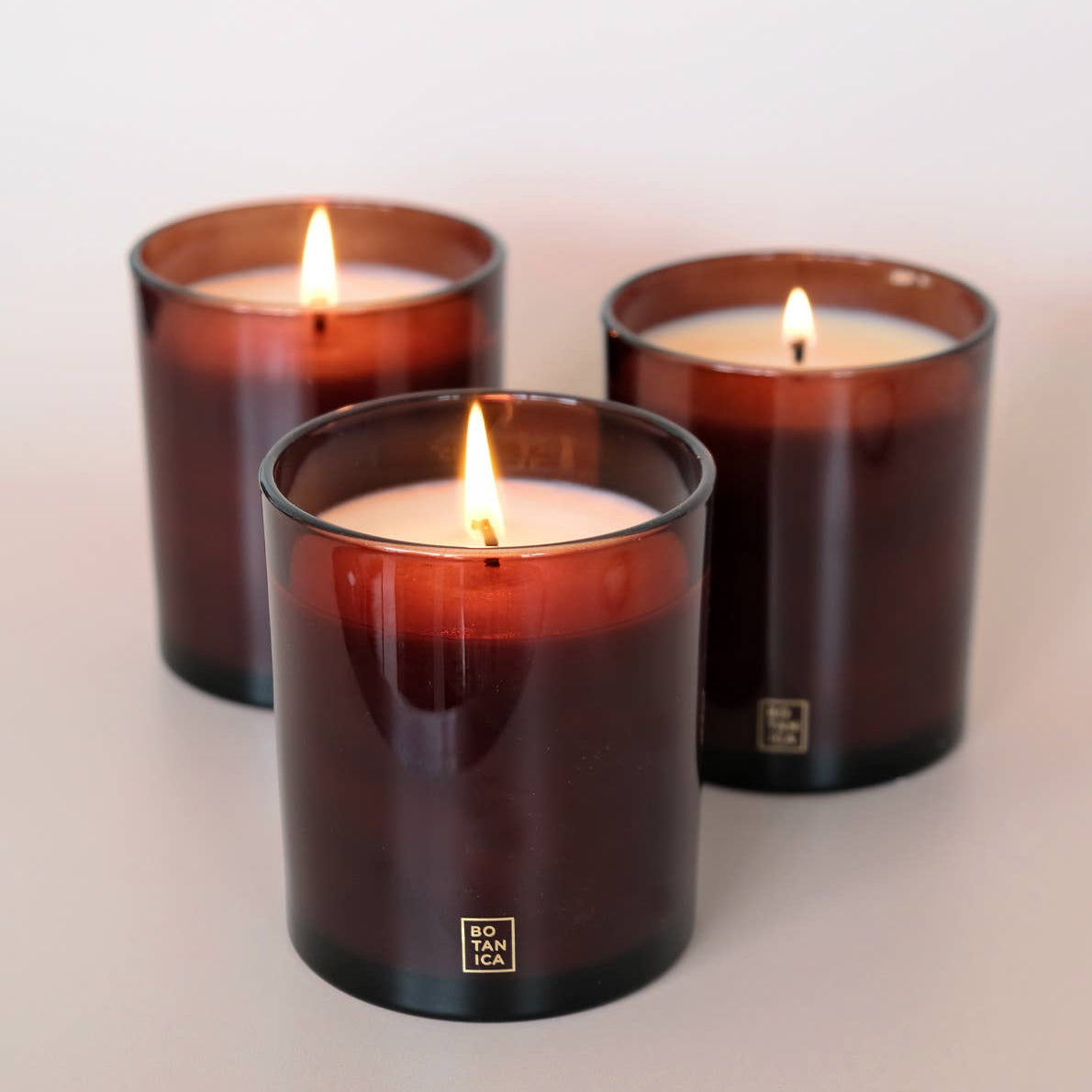 Three lit candles in brown glass containers on a light background