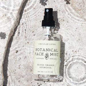 Botanical face mist bottle on a textured stone surface with flowers.