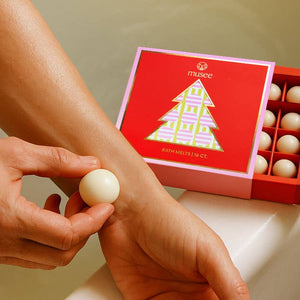 Person applying a white bath bomb to their wrist with a red 'musee' box in the background.