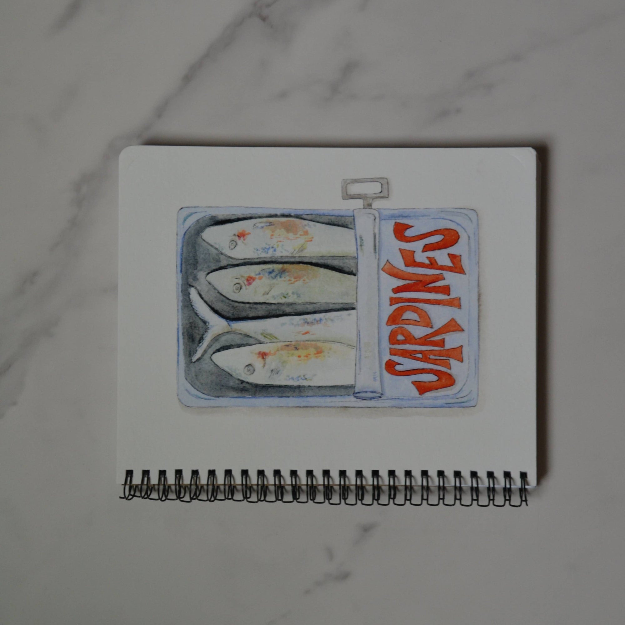 Small notebook with a sardine illustration on a marble surface