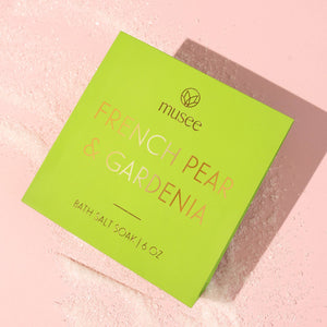 Green packaging of musee French Pear & Gardenia bath salts soak on a pink textured background