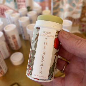 Hand holding a product labeled 'The Repair' with a colorful background of similar items.