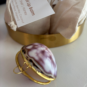 Lip balm in a shell packaging with a gold lid on a white surface.