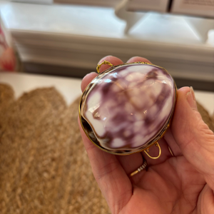 Hand holding a compact mirror with a purple and white design, blurred background