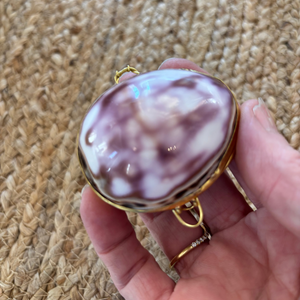Hand holding a marbled purple and white compact mirror against a textured beige background