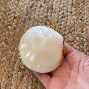 Hand holding a round, white object with gold trim against a textured beige background