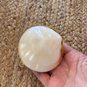 Hand holding a round, white object with gold trim against a textured beige background