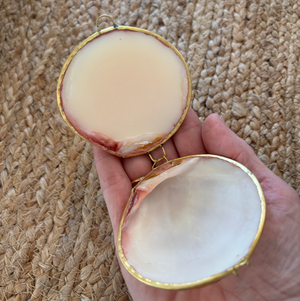 Hand holding a small open shell with a textured woven mat in the background