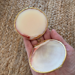 Hand holding a small open shell with a textured woven mat in the background