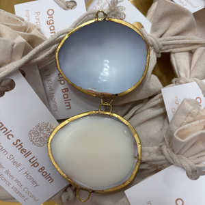 Two organic shell lip balms in gold cases on a textured surface with branded cards.
