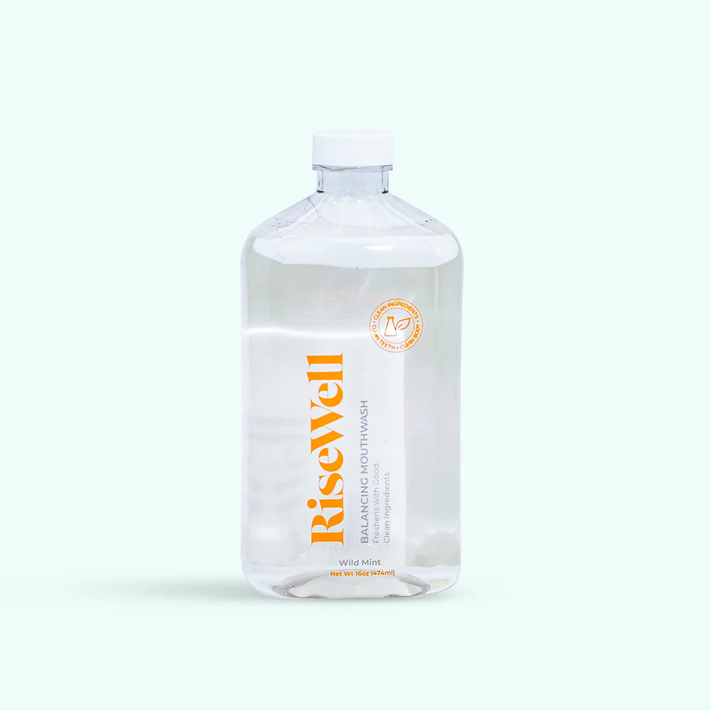 A clear bottle of Risewell Balancing Mouthwash with a white and orange label, cap visible at the top, on a white background.