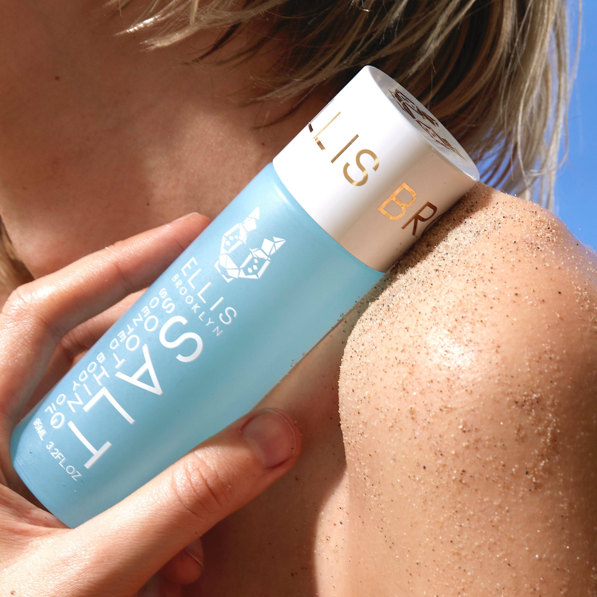 Person applying a blue bottle labeled 'SALT' to their shoulder against a clear blue sky.