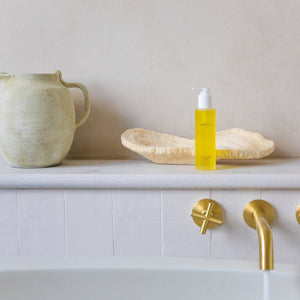Yellow bottle on a bathroom counter with gold fixtures and a beige wall.