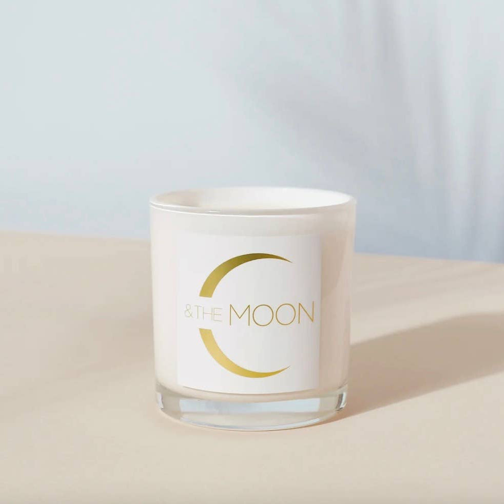 Candle in a glass jar with 'By the Moon' branding on a light background