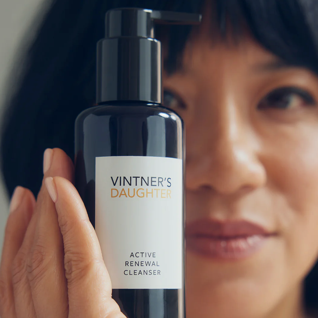 A woman holding a bottle of Active Renewal Cleanser in front of her face. 