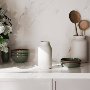 A Vitruvi air diffuser on a marble surface with decorative bowls and a plant.