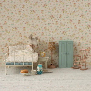 Miniature bedroom setup with a bed, cabinet, and toys against a floral wallpaper background.