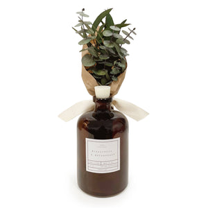 A brown glass apothecary bottle with a white bow and eucalyptus sprigs in the top