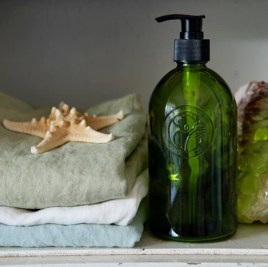 A green koala eco apothecary reusable pump bottle, next to a stack of linens and a starfish
