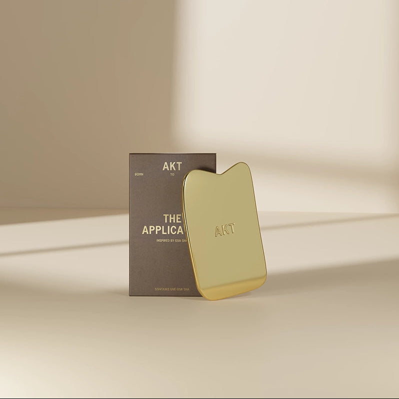 Gold Gua Sha tool with packaging on a beige background