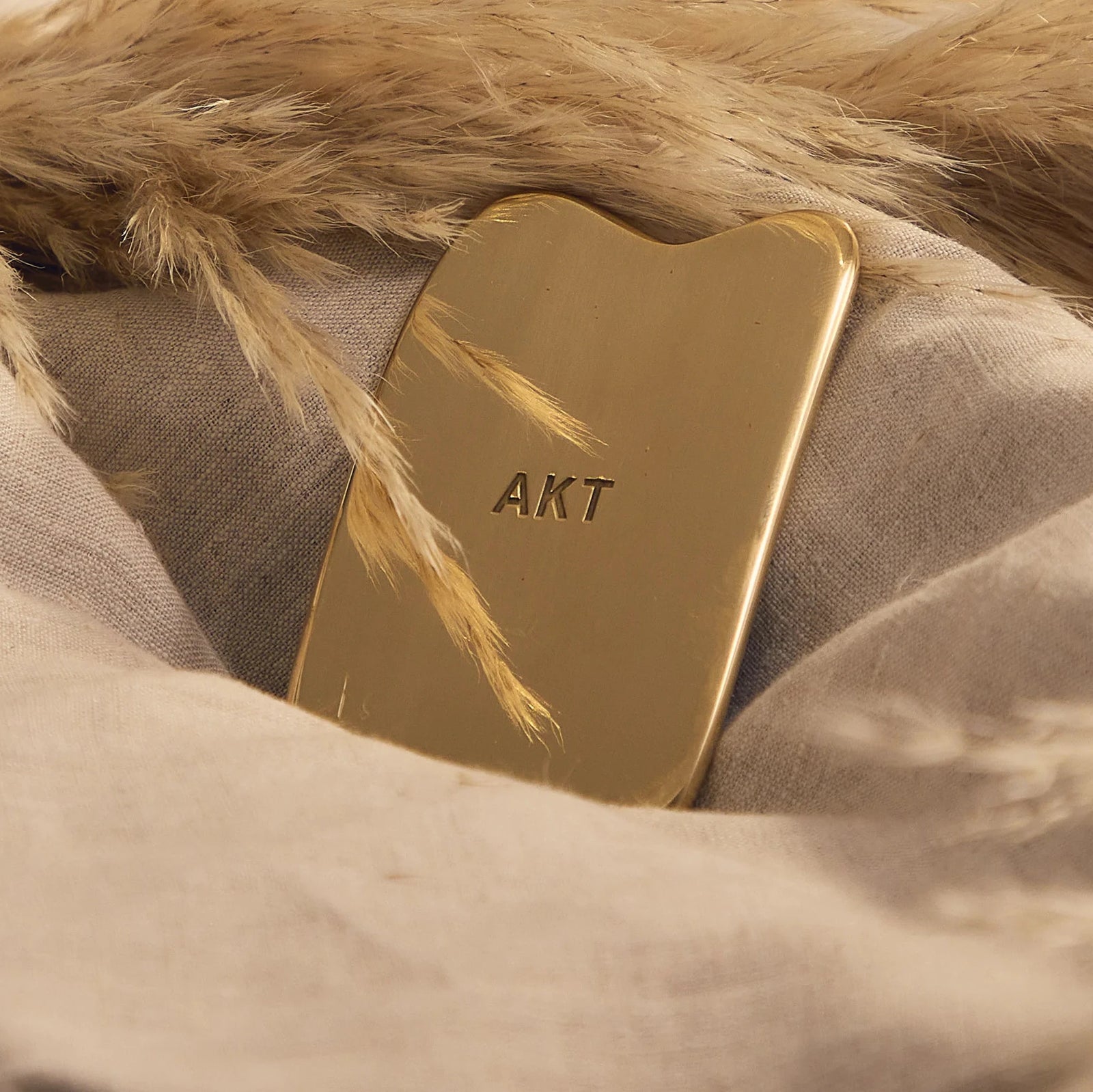 Gold Gua Sha tool with packaging on a beige background