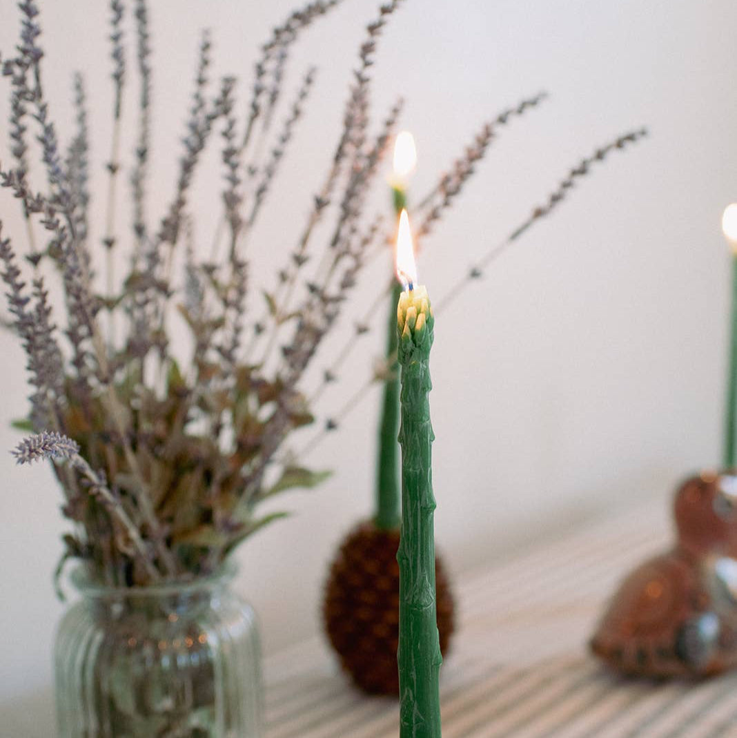 An asparagus candle on a table, with a vase of lavender behind it