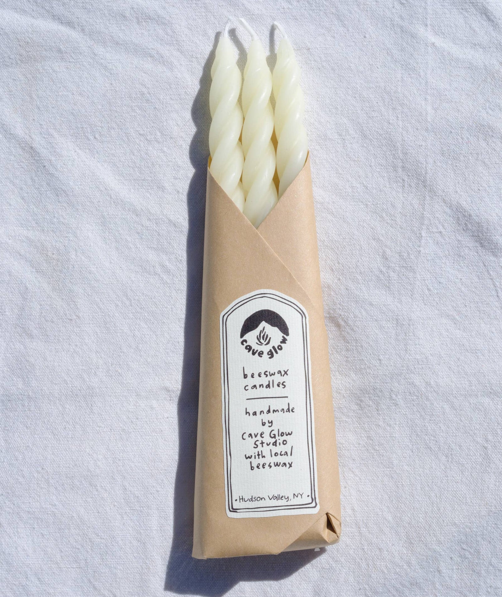 Beeswax candles in a brown paper bag on a white fabric background