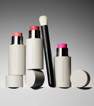 Set of cosmetic products including sticks and a brush on a gray background