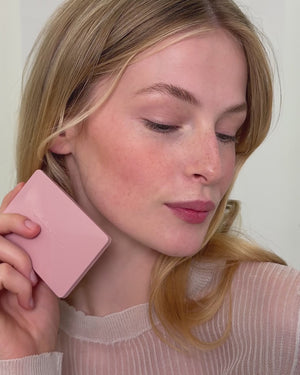 Woman holding a pink compact against her ear with a plain background
