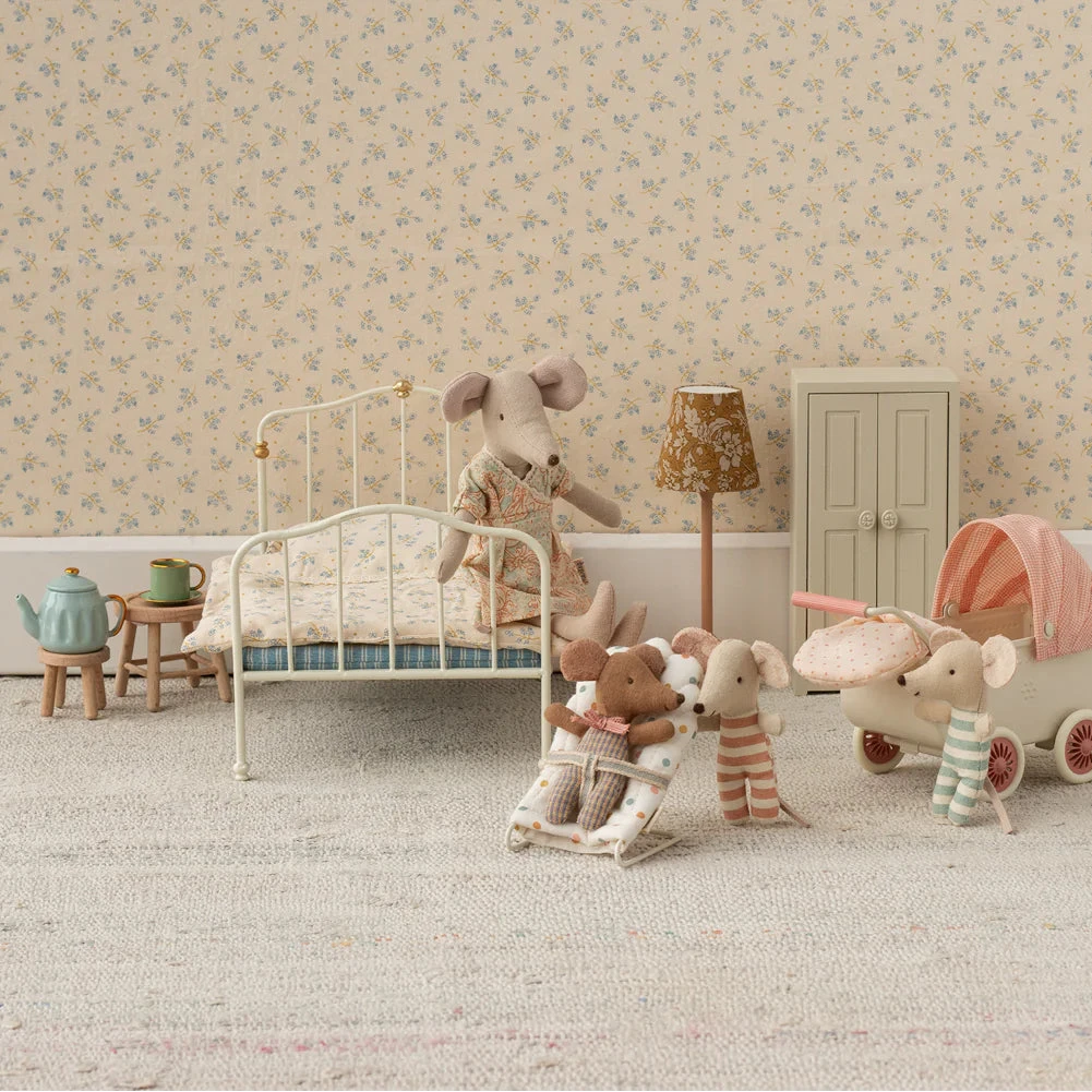 Miniature toy bedroom with stuffed animals and furniture against a floral wallpapered wall.